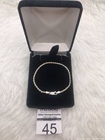 Silver twisted rope style bracelet displayed coiled inside a black velvet jewelry box with gray fabric lining.