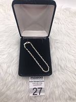 Sterling silver chain bracelet displayed inside a black velvet jewelry box on a white textured background, showing the chain links and lobster clasp.