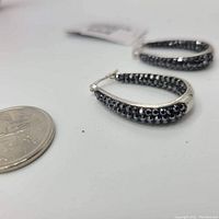 Close-up angled view showing one earring with marcasite star-shaped stones embedded in silver hoop next to Canadian quarter for size context.
