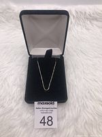 Sterling silver necklace displayed in an open black jewelry box with gray interior lining on a white fuzzy surface.