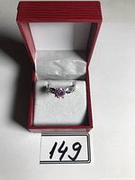 Photo showing sterling silver ring with single round cut pink stone in red ring box with white cushion.