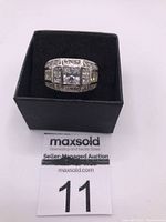 Top view of sterling silver ring with clear zirconia stones in box with auction lot label
