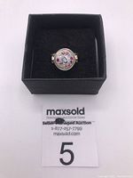 Front view of sterling silver ring showing round top adorned with multicolored rhinestones inside a black ring box.