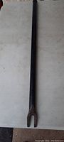 Full view of antique heavy steel tool, straight shaft with U-shaped forked end, approximately 20 inches long.