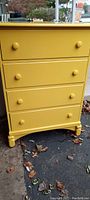Front view of the yellow painted antique hardwood dresser showing four drawers and round knobs.