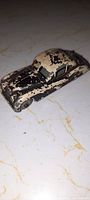 Top angled view of an antique small steel toy car, black and cream paint heavily chipped and worn.