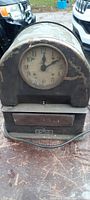 Full front view of antique timecard machine, showing clock and timecard slot, with worn paint and some rust on metal surface.