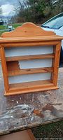 Full front view of the antique pine wall display unit showing the arched top, three shelves, and white textured back panel.