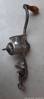 Full side view of antique steel meat grinder with wooden crank knob showing embossed branding and clamp base