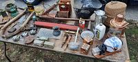 Wide shot showing full assortment of barn antiques and farm-related primitive items spread on a table including tools, lanterns, dice, cans, and ceramics.