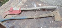 Two barn/farm axes with solid wood handles shown together on a surface, one with red metal blade cover, both used and weathered.