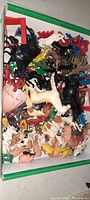 Top view of mixed collection of plastic animal figures and accessories including cows, pigs, horses, human characters, and playset elements inside a box.