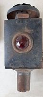 Front view showing circular red reflector set in black metal housing with visible patina and rust.