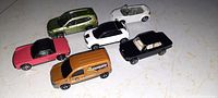 Six metal toy vehicles arranged on a surface showing a variety of colors and styles including hatchback, convertible, pickup truck, sports car, delivery van, and compact car.