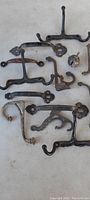 Photo showing antique steel door hooks, cloth hooks, and small auger with wooden handle arranged on a white surface, indicating condition as barn found with visible rust and patina.