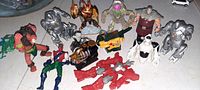 Lot of 11 transformer-type action figures arranged on white surface, showing various robot and creature designs in silver, red, green, brown tones.