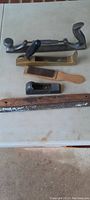 Photo showing six antique woodworking files and hand tools: large heavy file, wooden scrapers, metal hand plane, and wooden ribbed scraper with paint wear.