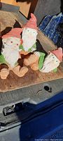 Three older decorative garden gnomes seated together on wooden surface, showing front and side views with bold colors and details.