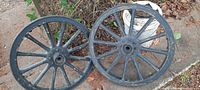 Pair of 24-inch black steel wagon wheels laying on ground outside, showing full wheel and steel outer rim