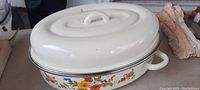 Photo of white enamel roaster pan with colorful floral design on the outside and matching lid with handle.