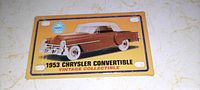 Front view of a small metal license plate style tag depicting a brown 1953 Chrysler Convertible with white top on a yellow and blue background. Text includes year, make, model, and 'Vintage Collectible'. The tag has four mounting holes in corners and shows minor surface scratches.