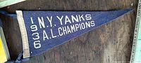 Full view of the small triangular navy blue felt pennant with white felt lettering showing '1936 N.Y. YANKS A.L. CHAMPIONS' on a wooden surface.