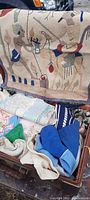 Antique leather suitcase open showing assorted vintage sewing materials including hand-sewn and embroidered patches and fabric pieces in various colors and patterns.