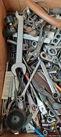 Box filled with various hand tools including wrenches, ratchets, sockets, pliers, and a wire brush.
