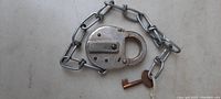 Metal Western Maryland Railroad padlock with attached chain and key laying flat on a surface, showing front side of the lock and key.