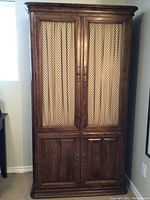 Front view of the Ethan Allen wooden armoire showing the fabric paneled upper doors and solid wood lower doors.