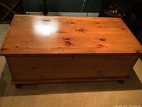 Front angled view of rectangular wooden blanket chest showing natural wood grain and knots with visible scratches on the top surface.