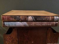 Two large books stacked horizontally showing spines labeled Volume One and Two of The Sistine Chapel.