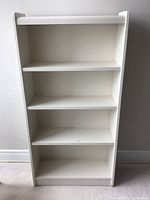 Front view of the white bookshelf showing four shelves and signs of wear.