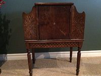 Front view of the entire wooden cabinet showing carved floral designs on side panels, front door, and legs.