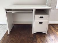 Front view of the white wooden desk showing keyboard tray and two drawers with black handles.