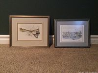Two framed nautical art prints placed on carpet against dark wall; showing full view of both pieces.