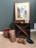 Photo showing entire lot including pottery jug with hole, metal milk can, wooden crate, painting, wooden animal sculpture, green glass dish, and small figurine.