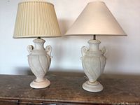 Pair of two vintage urn-shaped table lamps standing side by side on a wooden surface with different fabric shades, one showing minor repair.