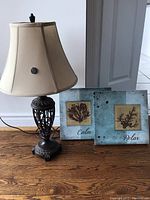 Decorative table lamp with cream shade and two coastal-themed wall art pieces on wood floor