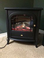 Front view of the black Dimplex electric wood stove heater plugged into power and showing glowing ember lights inside.