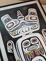 Close-up of painted metal art plaque showing stylized Haida beaver face with traditional indigenous formline patterns in black, white, red, and gold.