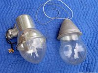 Both vintage industrial light fixtures placed on a blue quilted cloth showing the overall condition and size for reference.