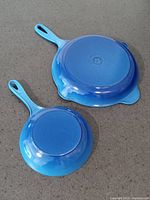 Both skillets bottom-side up showing blue exterior and manufacturer stamp