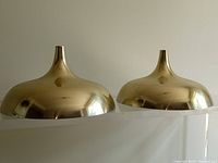 Side view of two vintage gold tone aluminum pendant light shades showing rounded domed bodies with narrow neck openings.