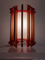 Front view of vintage mid-century modern table lamp powered on showing glow through white cylinder diffuser and wooden slats around it.