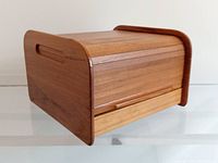 Vintage teak tambour roll top storage box shown closed from an angle highlighting wood grain and rounded edges.
