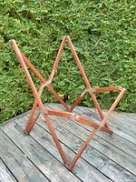 Side angle of vintage teak folding Tripolina chair frame showing wood slats and metal hinges on deck outdoors