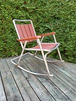 Side angled view of vintage mid-century modern folding rocking chair showing aluminum frame with wood slats on seat, back, and armrests, and curved rockers at base.