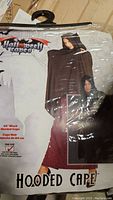 Packaged black hooded cape labeled as Halloween Capes brand, showing model wearing the cape for size reference.