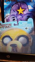 Close-up photo showing Jake character glasses in original packaging with Adventure Time logo and age warning.